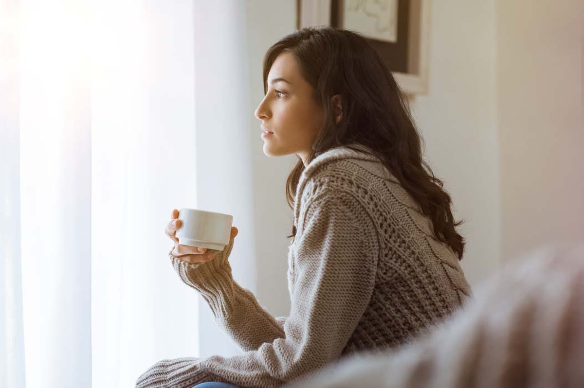 Woman sitting quietly by a window with coffee, reflecting - representing self-searching and inner awareness